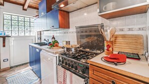 A kitchen with a gas stove, wooden cabinets, and a window with a view. - Casa Rolè, Lake Maggiore Patio House w/ BBQ, Dormelleto, Italy (Dormelleto)