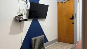 Een kamer met een tv aan de muur, een radiator, een houten deur en een bank met kussens.