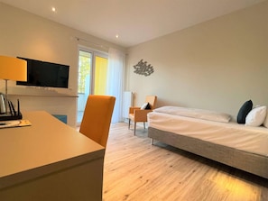 A modern hotel room with a bed, a desk, a chair, a TV, and a window. - Bernsteinsee Hotel and Ferien Room With Balcony (Sassenburg)