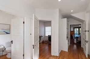 A spacious hallway with white doors leading to various rooms, a visible laundry area, and a dining area with natural light. - Hollywood Heritage  Villa (Los Angeles)