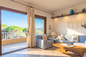 Un salon comprenant un canapé, des fauteuils, une table basse, une lampe et une vue sur la verdure et les montagnes.