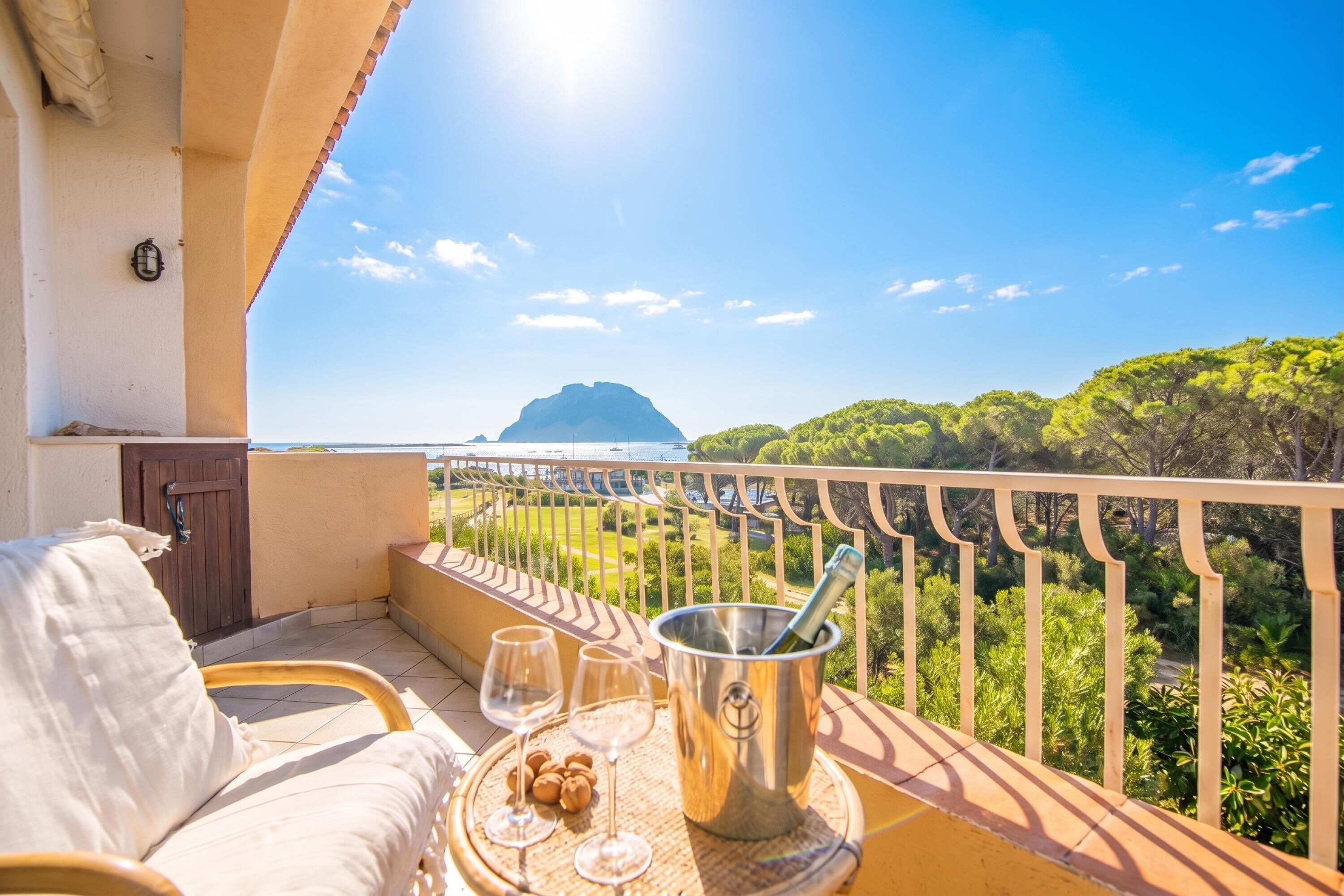 A balcony with a view of a mountain, a table with glasses and a bottle, and a sofa.