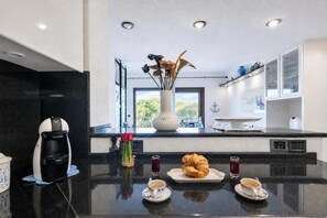 Eine moderne Küche mit Kaffeemaschine, Blumen in einer Vase und einem Croissant auf einer Arbeitsfläche.