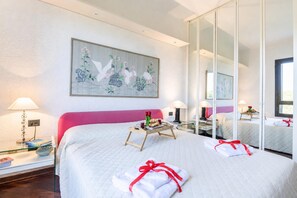 Una camera d'hotel con un letto grande, un comodino con una lampada, una pianta sul comodino e un quadro appeso al muro.