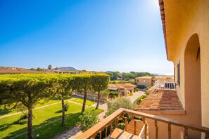 A balcony with a view of a courtyard, a building with a terracotta roof, and a clear blue sky. - Il Vecchio Faro 66, Porto San Paolo, Italy (Porto San Paolo)