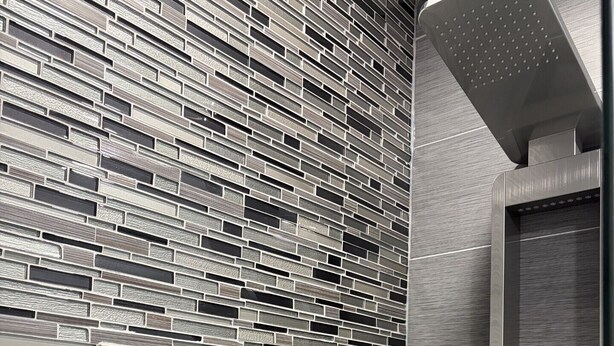Un baño moderno con pared texturizada, ducha integrada y panel de control.