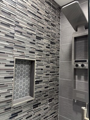 A modern bathroom with a textured wall, a built-in shower, and a control panel.