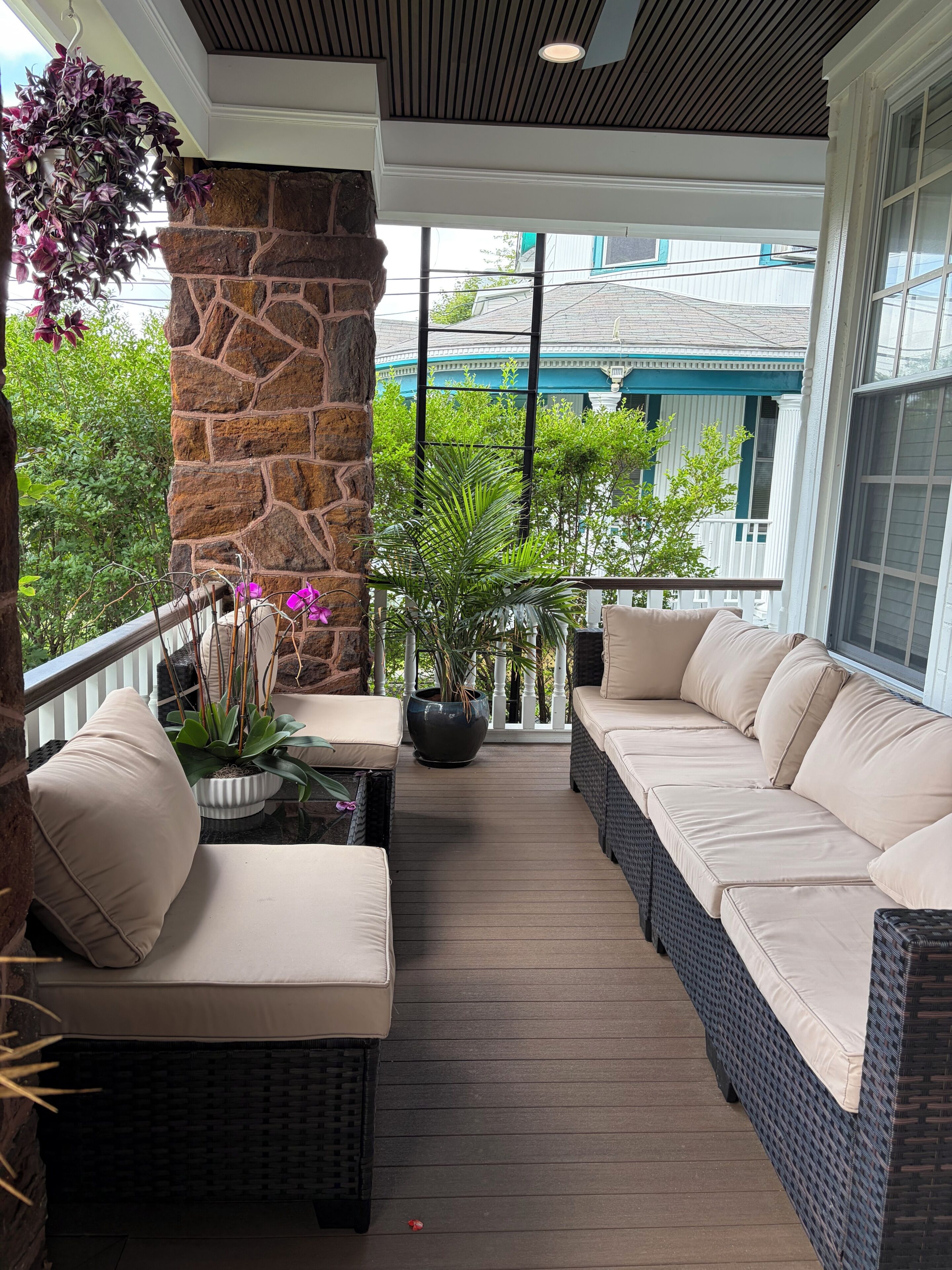 A covered porch with wicker furniture, a stone wall, and potted plants.