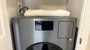 A compact, stainless steel washing machine in a narrow hallway with a tiled floor. - Spacious Luxury Apartment in Restored Asbury Mansion (Asbury Park)