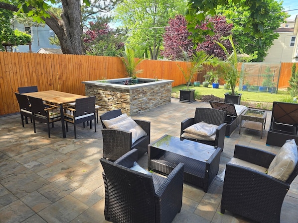Une terrasse extérieure avec un foyer en pierre, des meubles en osier et une clôture en bois.