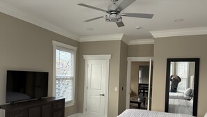 A bedroom with a bed, a dresser, a TV, a ceiling fan, and a door. - Spacious Luxury Apartment in Restored Asbury Mansion (Asbury Park)