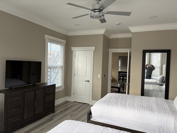A bedroom with a bed, a dresser, a TV, a ceiling fan, and a door.