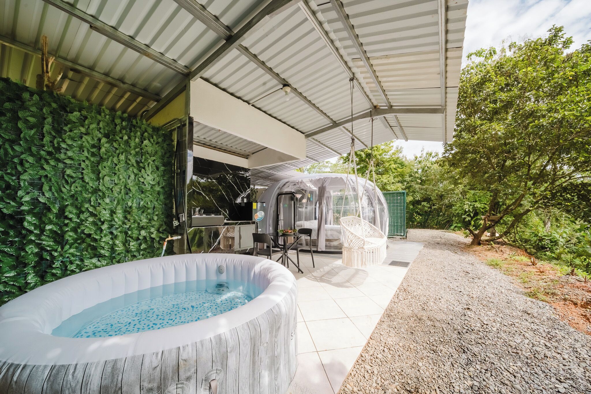 Un espace extérieur abrité comprenant un jacuzzi, un coin salon couvert et un mur recouvert de verdure.