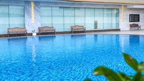 An indoor swimming pool with clear blue water, benches along the edge, and a glass wall in the background. - Enrich Grand Hotel (Bangkok)