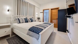Une chambre moderne avec un grand lit, des tables de chevet, une télévision et une salle de bain visible à travers une porte ouverte.