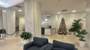 A modern lobby with marble walls, a reception desk, a Christmas tree, and a seating area with a black coffee table. - Modern & cozy apartment beachfront (Sunny Isles Beach)