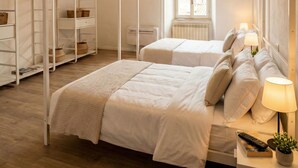 A bedroom with two beds, a wardrobe, and a bedside table with a lamp and remote control. - Le Volte di via Portica (Assisi)
