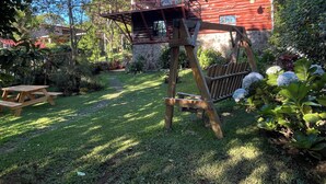Una estructura de madera rústica con balcón, rodeada de abundante vegetación y un muro de piedra.