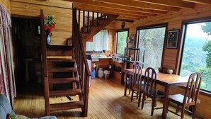 Interior de una cabaña de madera con comedor, cocina y una escalera que sube a un altillo.