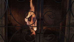 Una chimenea con una protección de metal y adornos en espiral, llamas visibles y un muro de piedra al fondo.