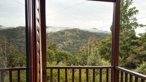 Una terraza de madera con una mesa redonda y taburetes, con vistas a un paisaje montañoso.