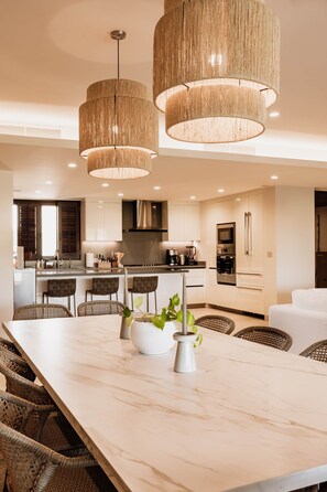 A modern kitchen with a central island, pendant lighting, and a dining area with wicker chairs.