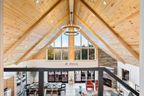 A spacious loft with a high ceiling, wooden beams, a chandelier, a fireplace, and a view of the outdoors.
