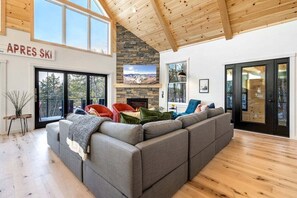 Un salon moderne avec un grand canapé d’angle, une cheminée en pierre et une vue sur l’extérieur.