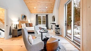 Ein modernes Interieur mit Holzbalkendecke, einem Bett, einer Sitzecke und großen Fenstern.