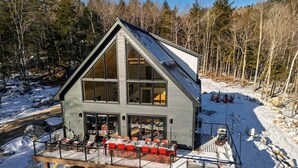 Eine moderne Hütte mit großer Terrasse, großen Fenstern und einem geneigten Dach.