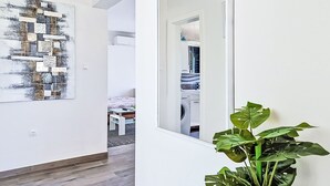 A hallway with a wooden floor, a large abstract painting, a potted plant, and a view into a bedroom with a bed and a washing machine. - Vacation home Sara by Interhome (Zadar)