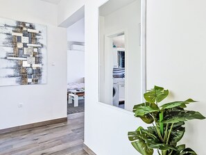 A hallway with a wooden floor, a large abstract painting, a potted plant, and a view into a bedroom with a bed and a washing machine. - Vacation home Sara by Interhome (Zadar)