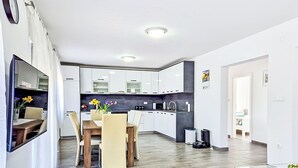 A modern kitchen with white cabinets, a dining area with a wooden table and chairs, and a small living space with a glass coffee table. - Vacation home Sara by Interhome (Zadar)