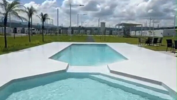 Una piscina moderna con diseño geométrico, rodeada de palmeras y un cielo despejado.