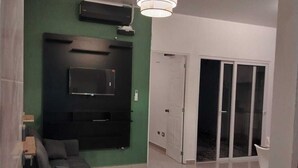 Una sala de estar moderna con un sofá seccional negro, un televisor de pantalla plana montado y una lámpara en el techo.