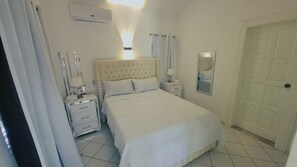 A bedroom with a bed, bedside tables, a mirror, and a door. - Villa Pelichini (Sosúa)