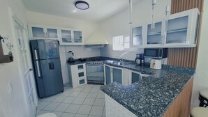 Una cocina compacta con armarios blancos, un refrigerador de acero inoxidable, estufa y pileta.