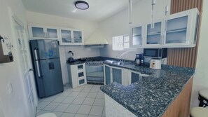 A compact kitchen with white cabinets, a stainless steel refrigerator, a stove, and a sink. - Villa Pelichini (Sosúa)