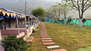 A pathway leading to a row of tents with a grassy area and swings on the right. - Sukhdev Resort Rishikesh (Rishikesh)