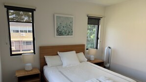 Una cama bien hecha con sábanas blancas y dos almohadas, con mesitas de noche con lámparas y un pequeño estante.