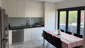 Una cocina moderna con armarios blancos, lavavajillas y un comedor con mantel a rayas.