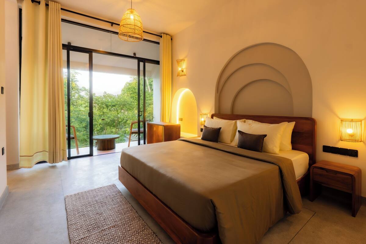 Un dormitorio amplio con una cama grande, vista a través de un ventanal corredero y una pequeña mesa con una silla.
