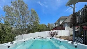 A hot tub in a backyard with a white fence, trees, and a house in the background. - Located in Basement of Twin Home. Relax & Play with Swim Spa & Game Room for 4 (Springville)