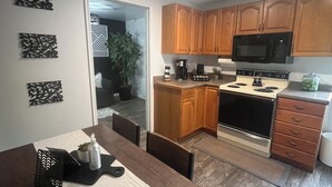 A modern kitchen with wooden cabinets, a microwave, a stove, and a dining area with a table and chairs. - Located in Basement of Twin Home. Relax & Play with Swim Spa & Game Room for 4 (Springville)