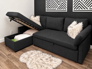 A modern living room with a sofa that has a built-in storage bench, a fluffy rug, and a wall with geometric art. - Art City Escape - Luxury Swim Spa & Private Entertainment Retreat (Springville)