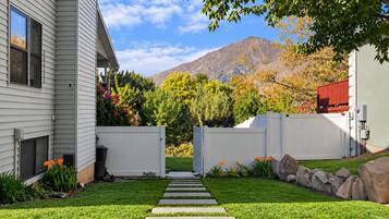 Un jardin bien entretenu, avec un chemin de pierres menant à une porte, entouré d’une végétation luxuriante et dominé par une chaîne de montagnes en arrière-plan.