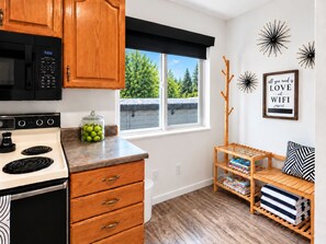A kitchen with wooden cabinets, a stove, and a window with a view of greenery. - Art City Escape - Luxury Swim Spa & Private Entertainment Retreat (Springville)