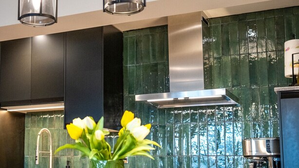 Une cuisine moderne avec des luminaires suspendus, un pare-feu vert et une composition florale fixée au plafond.