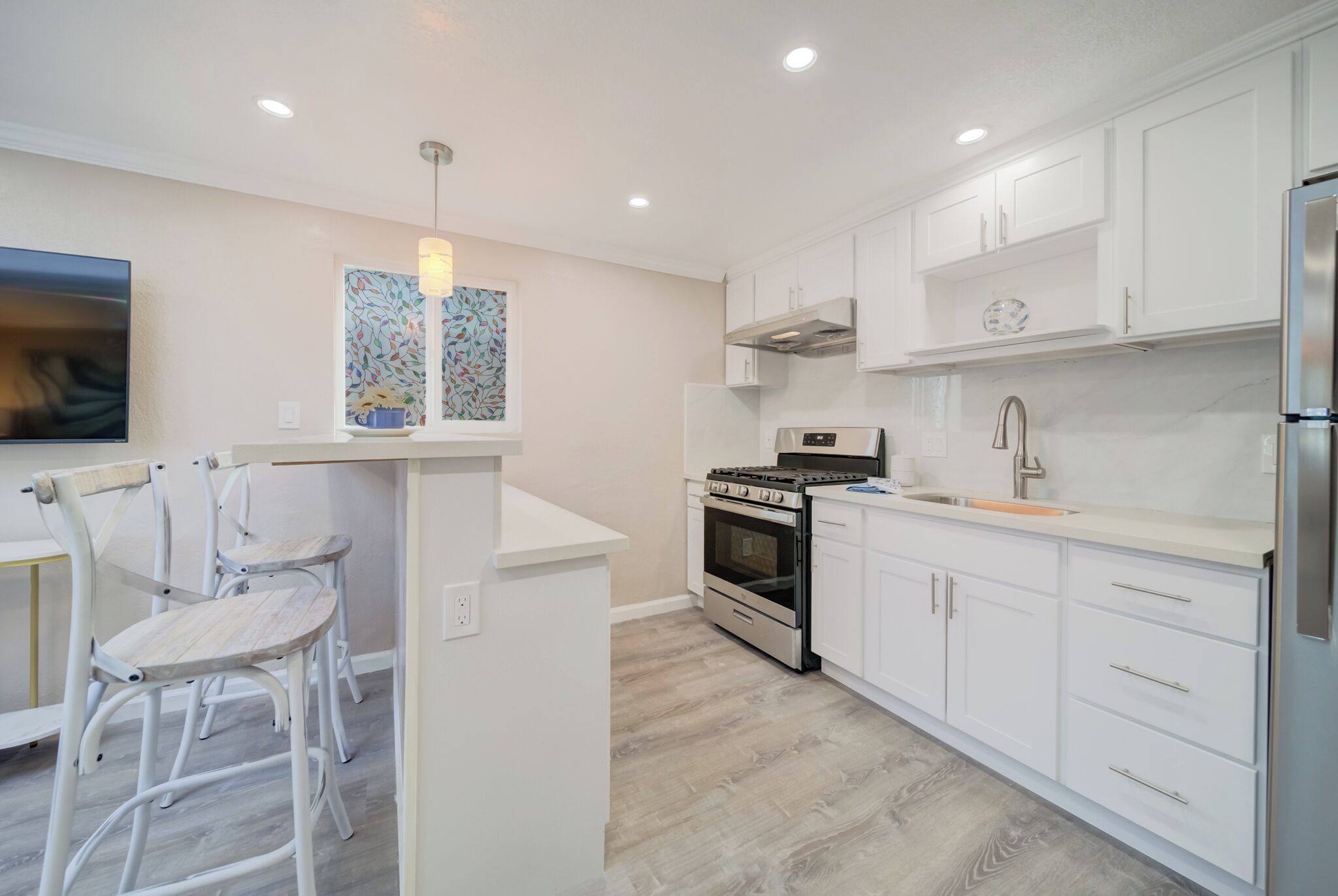 A modern kitchen with white cabinetry, a built-in oven, and a stainless steel refrigerator.