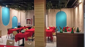 A restaurant with red tablecloths and chairs, a wooden reception desk, and decorative greenery. - The Perch Hostel (Olongapo)